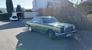 Ein grünes Auto parkt am Straßenrand vor einem Haus.