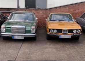 Zwei alte Autos stehen nebeneinander auf einem Parkplatz.