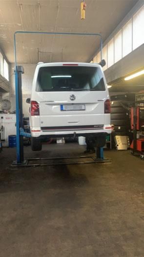 Ein weißer Lieferwagen steht auf einer Hebebühne in einer Garage.