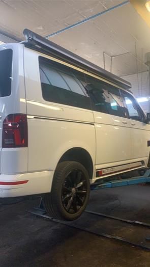 Ein weißer Lieferwagen steht auf einer Hebebühne in einer Garage.