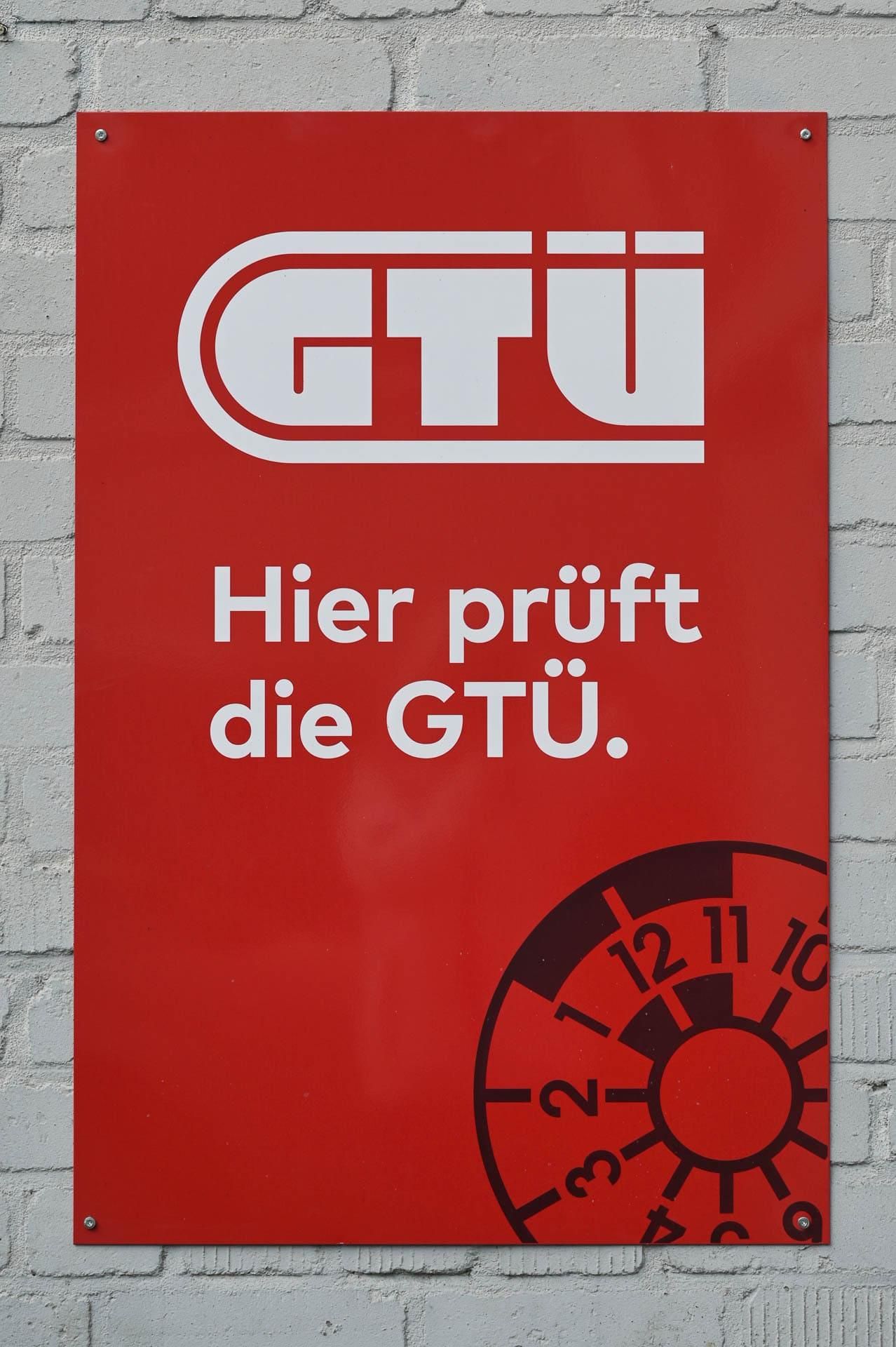 Ein rotes Schild mit der Aufschrift „Hier prüft die gtu“ darauf