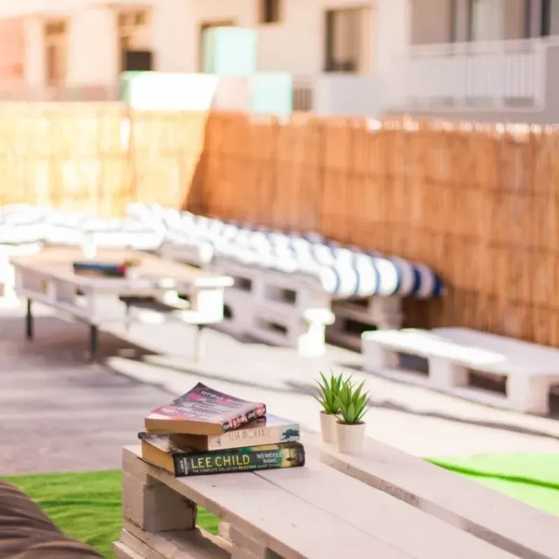 Libros sobre una mesa de palets blancos con bancos acolchados en una zona de salón al aire libre.