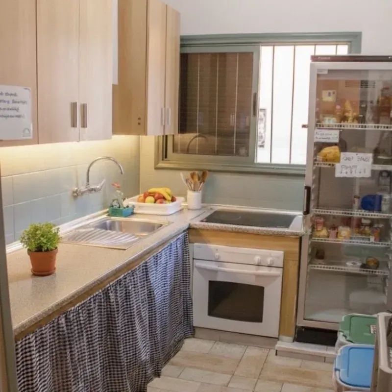 Cocina pequeña con gabinetes de madera clara, fregadero, estufa y refrigerador parcialmente abierto.