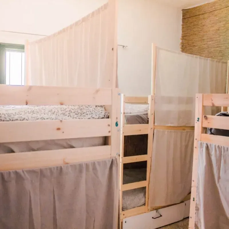 Literas en una habitación con marcos de madera de colores claros y cortinas para mayor privacidad.