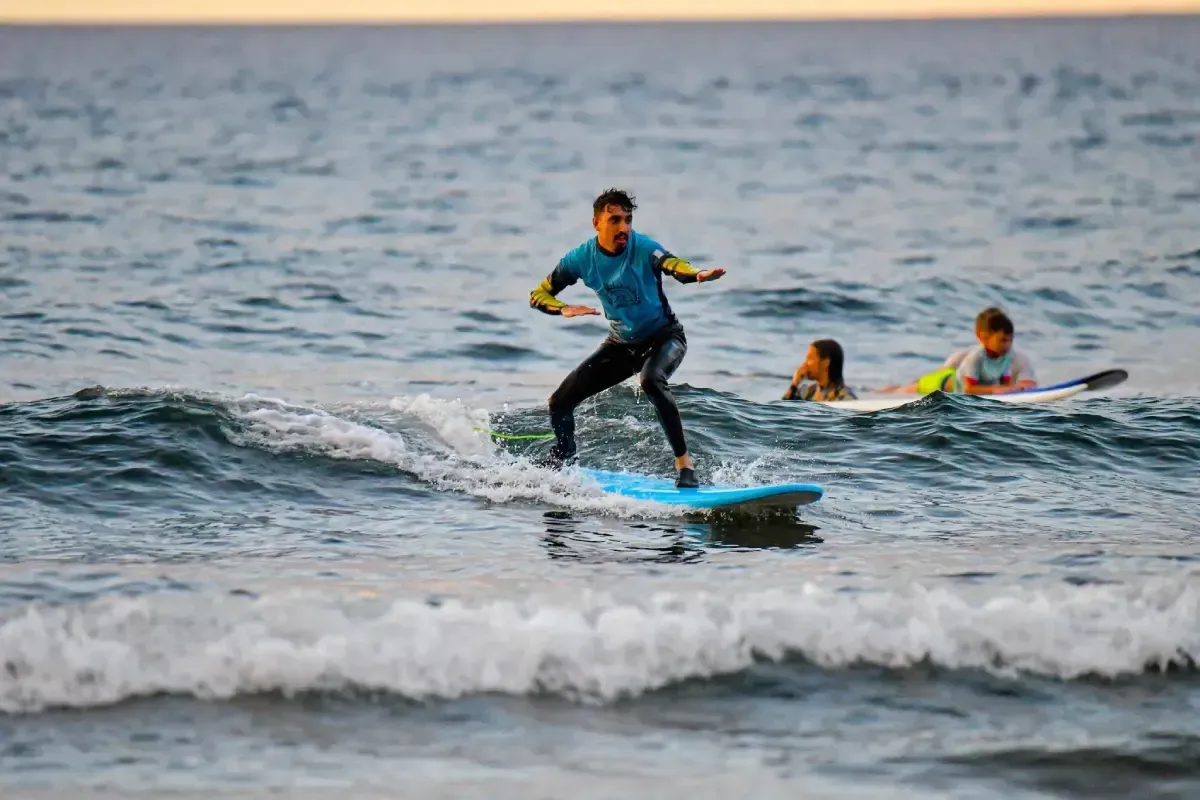 Hombre surfeando en una tabla de surf azul, otros dos en tablas al fondo, olas del océano.
