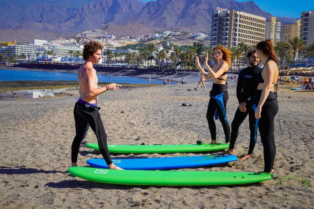 Grupo de personas en una playa con tablas de surf; una persona dando instrucciones a los demás.