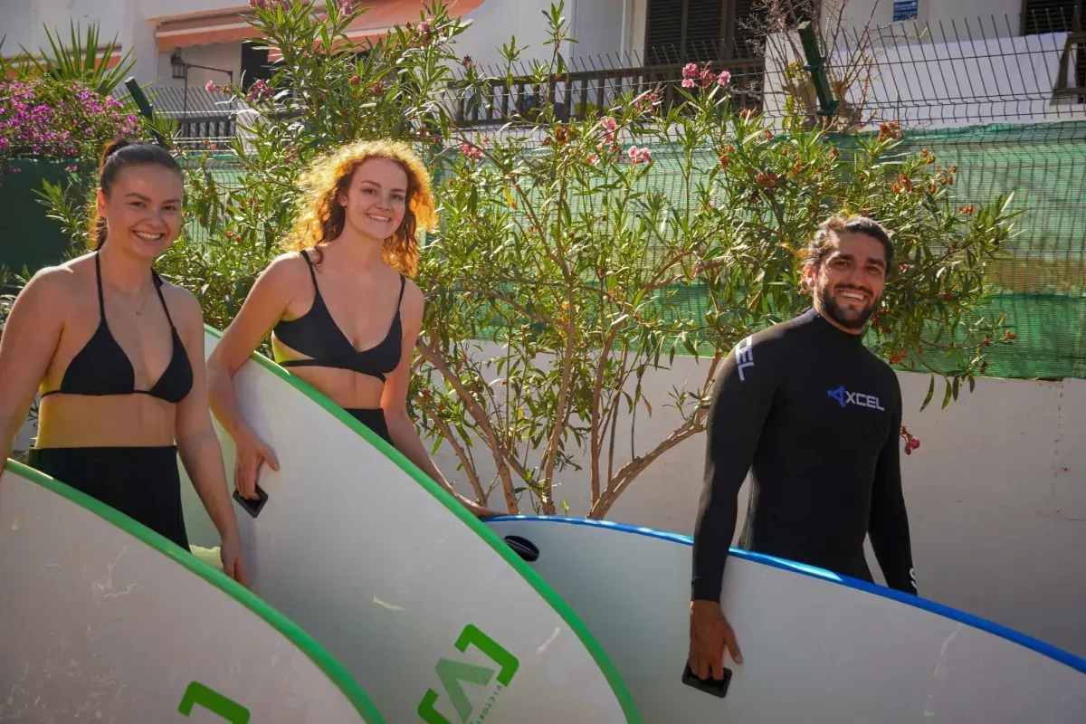 Tres personas sosteniendo tablas de surf sonríen al aire libre cerca de la vegetación.