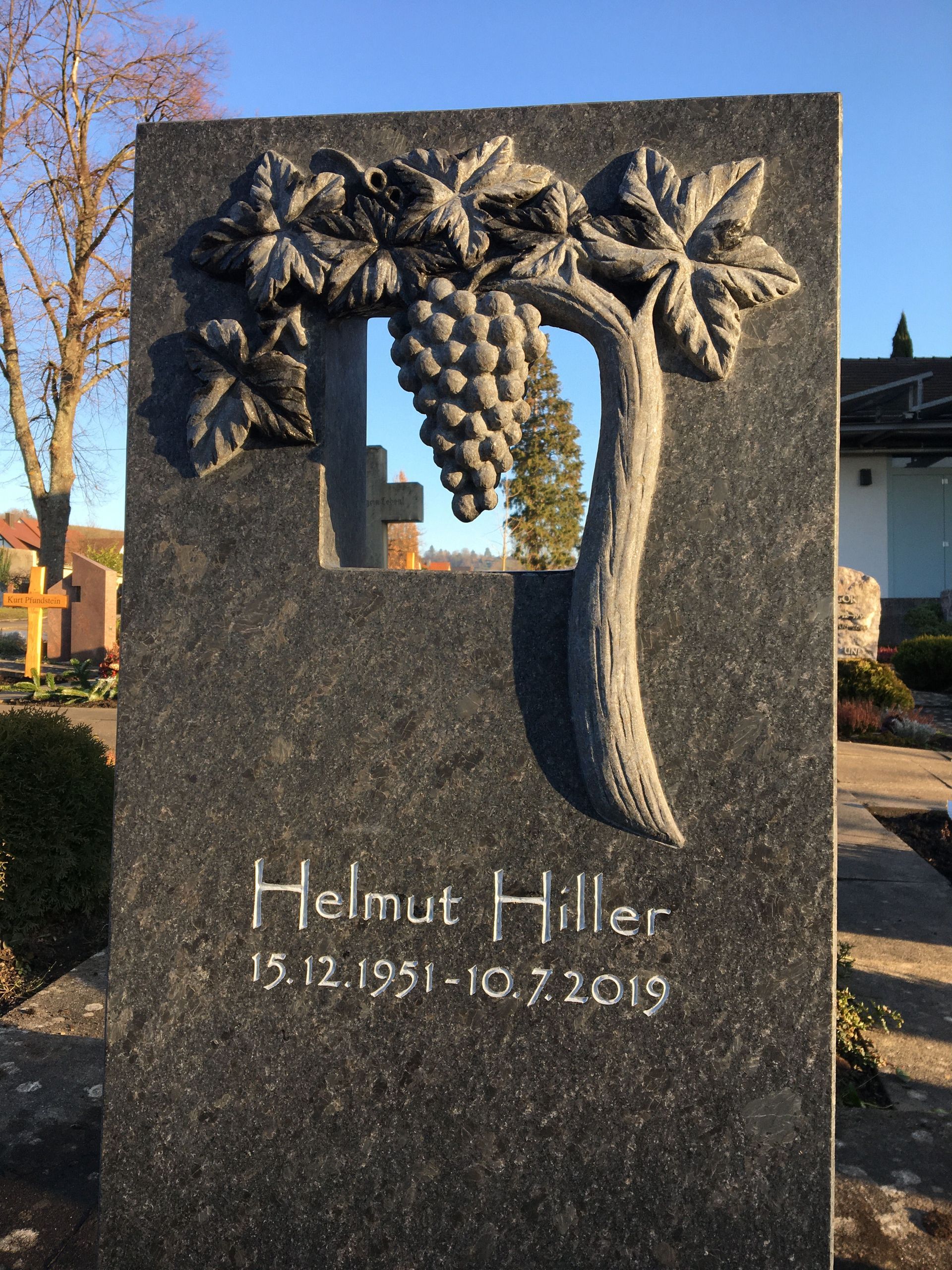 Ein Grabstein für Helmut Hiller mit eingeritzten Trauben und Blättern