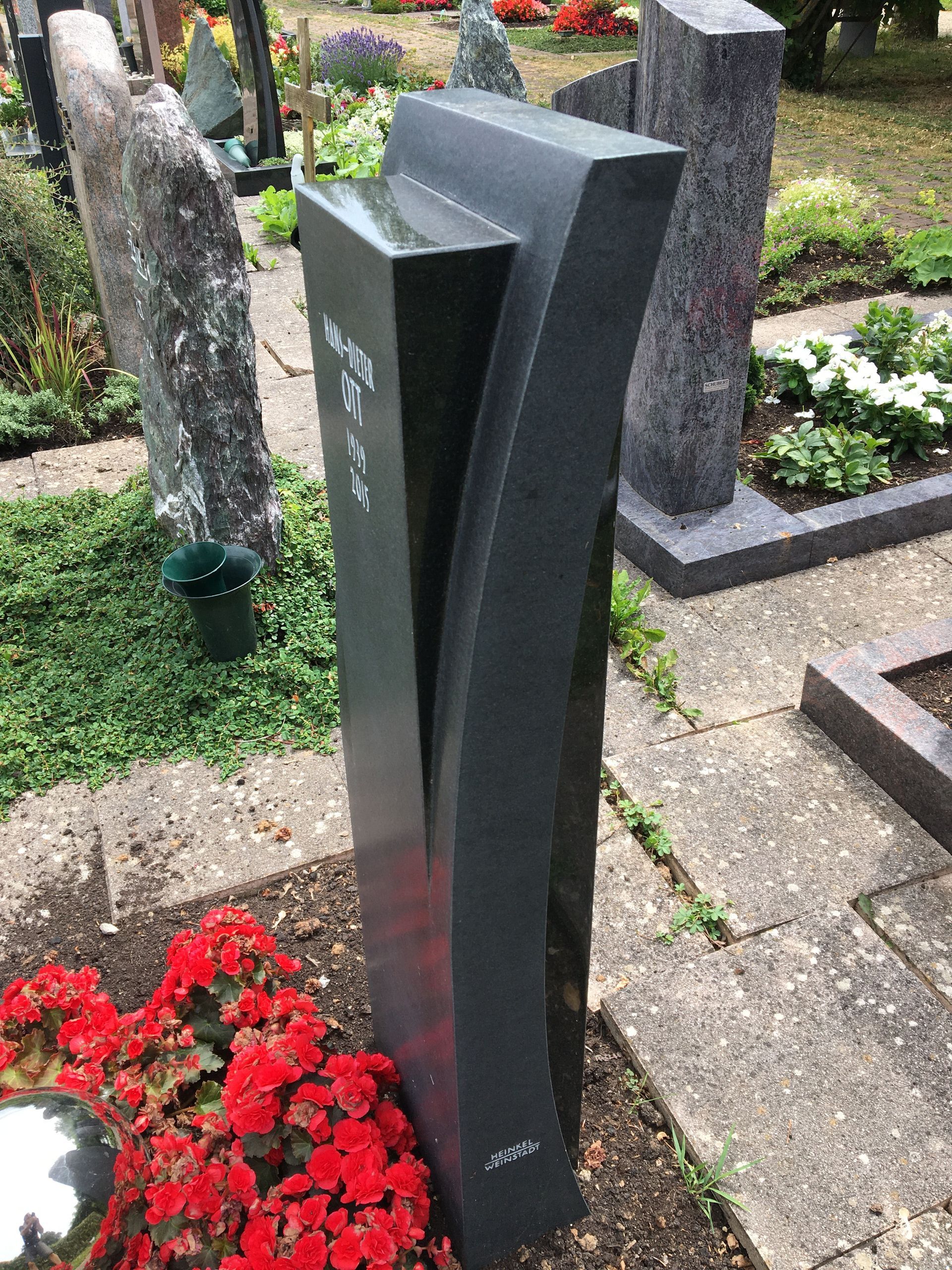 Ein Grabstein auf einem Friedhof mit roten Blumen davor.