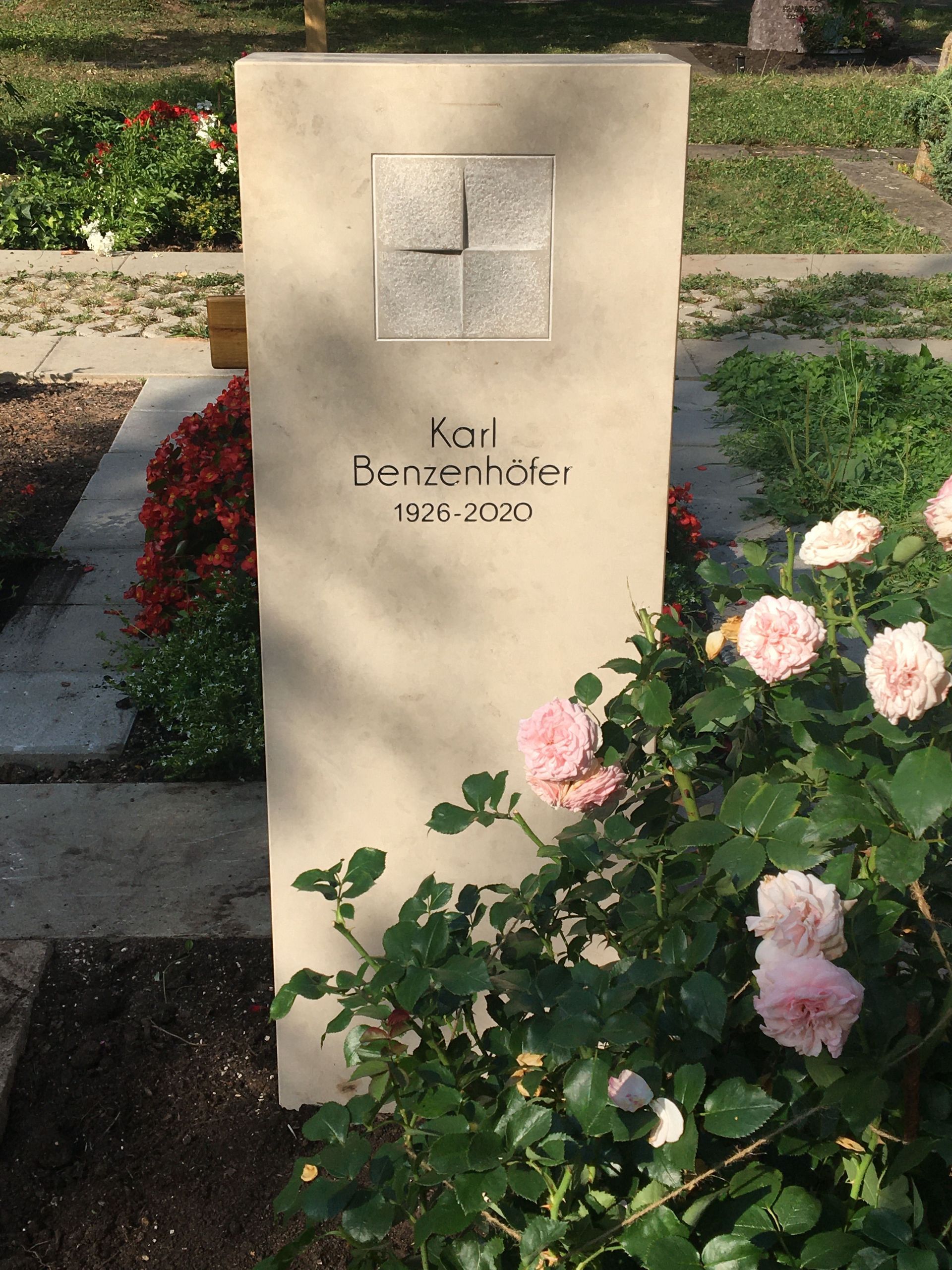 Ein Grabstein mit einem Kreuz darauf ist von Blumen umgeben.