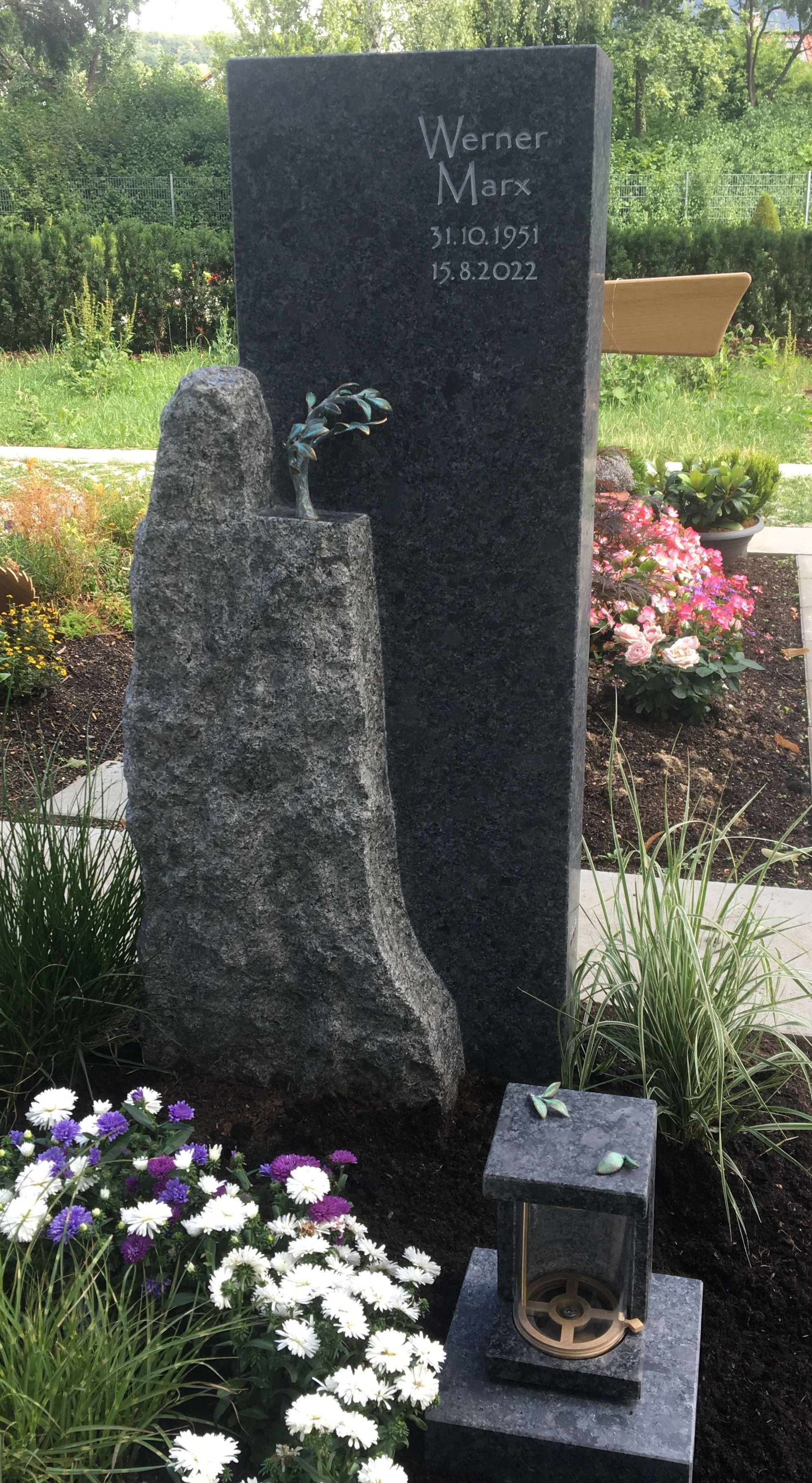 Ein Grabstein auf einem Friedhof mit Blumen und einer Laterne.