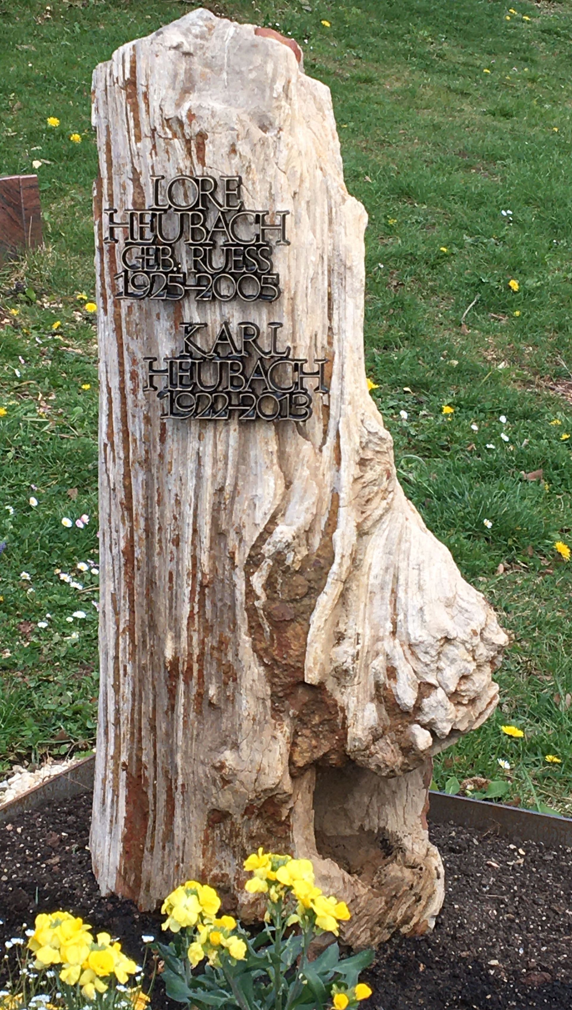 Ein Grabstein aus einem Baumstumpf mit gelben Blumen davor.