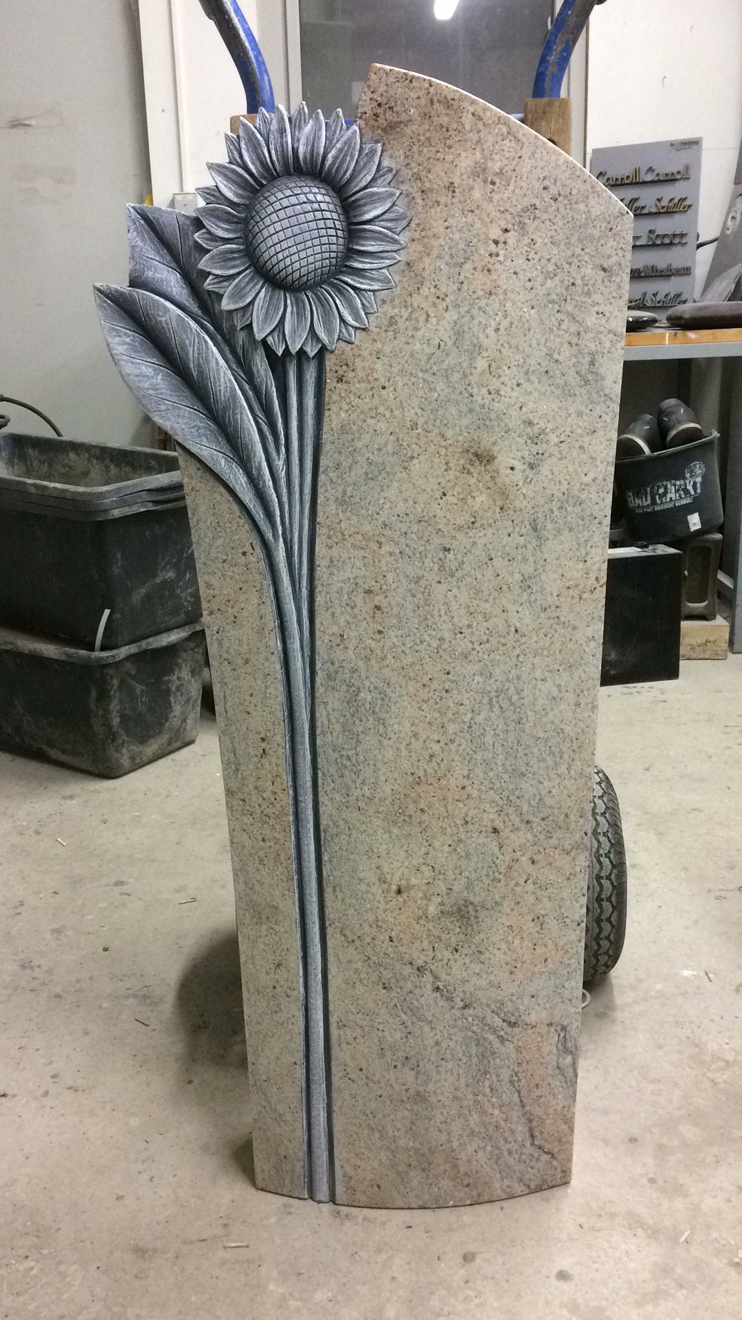 Auf dem Boden liegt ein Grabstein mit einer eingeschnitzten Sonnenblume.