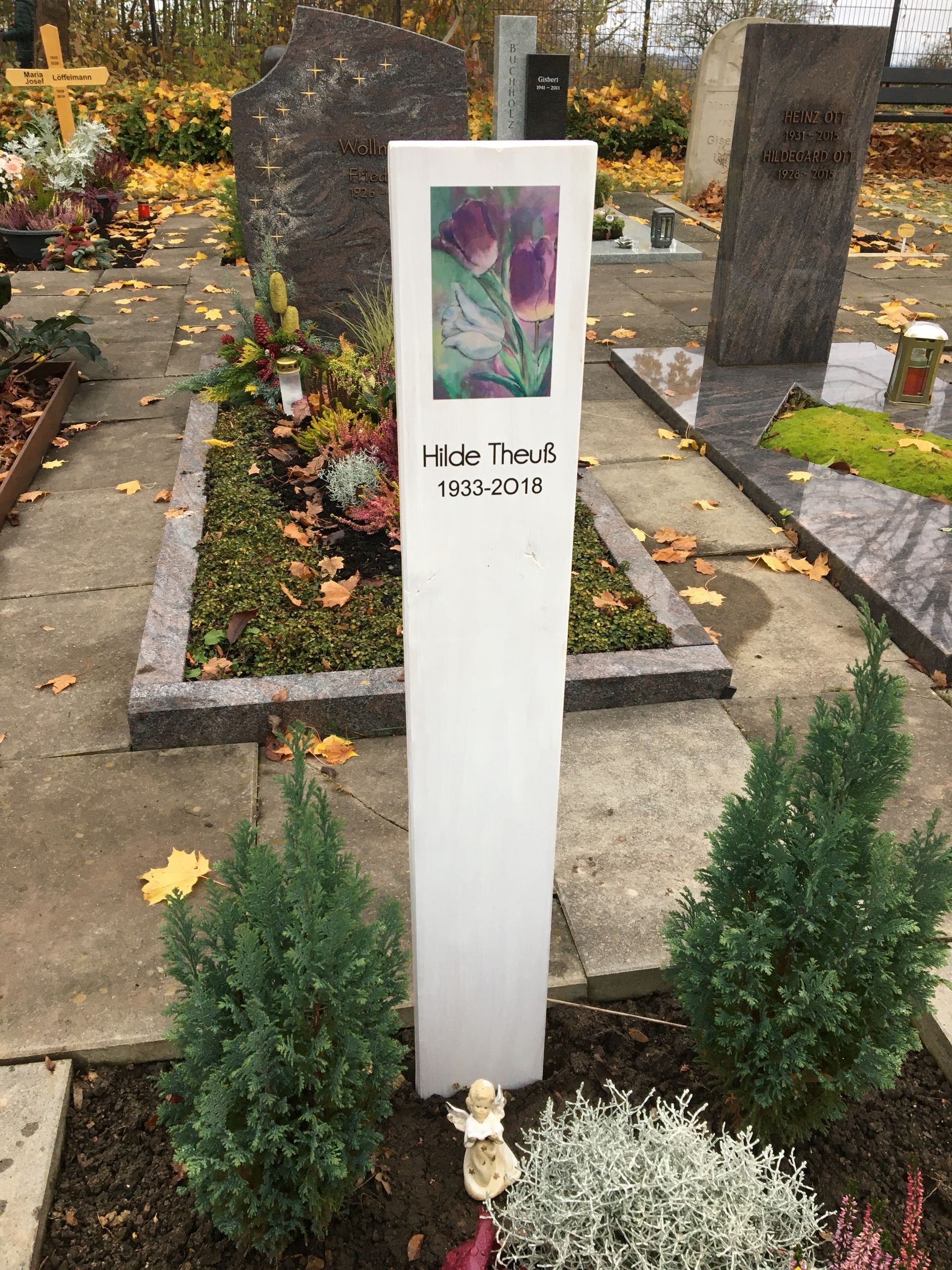 Ein weißer Grabstein mit einem Blumenbild darauf auf einem Friedhof.