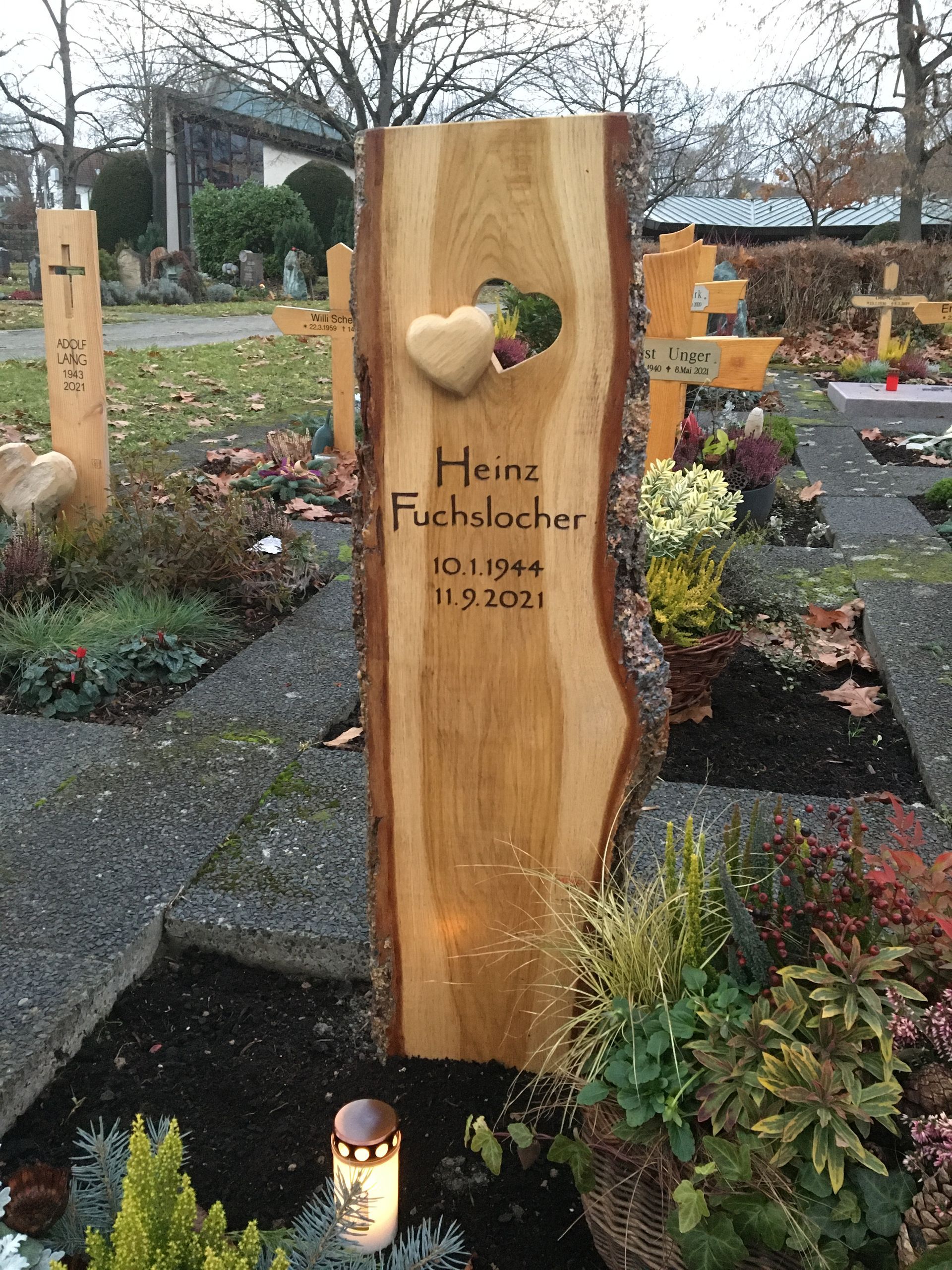 Auf einem Friedhof steht ein hölzerner Grabstein mit einem ausgeschnittenen Herzen.