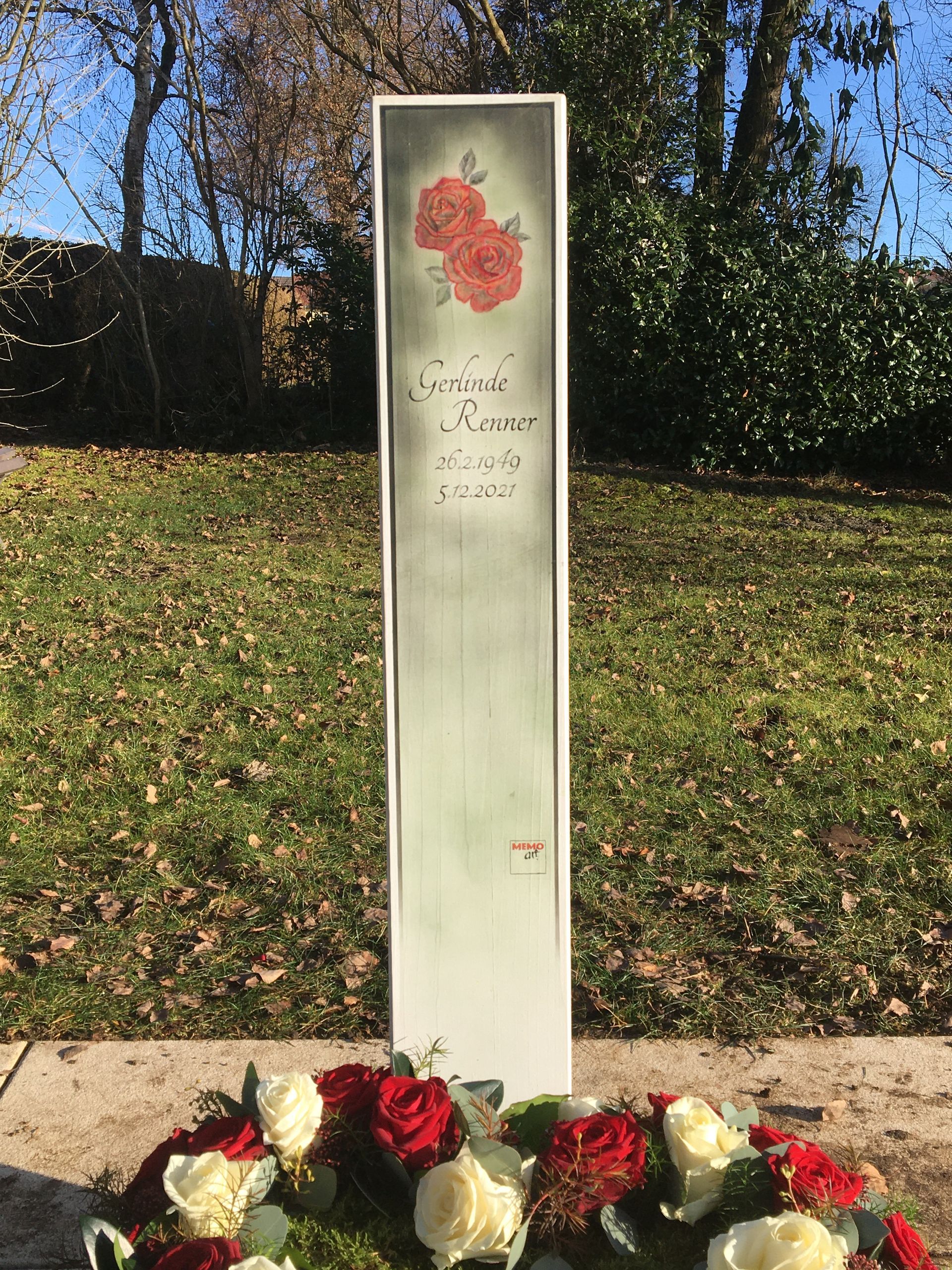 Ein weißer Pfosten mit einem Rosenbild darauf ist von Blumen umgeben.