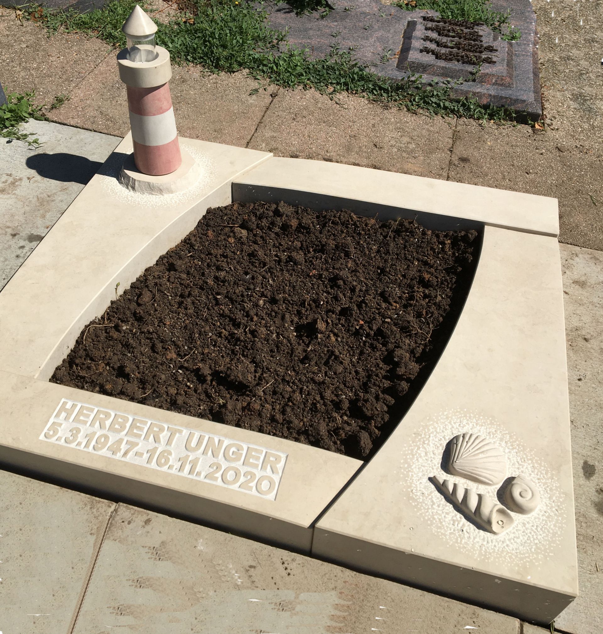 Ein Grabstein für Herbert Unger mit einem Leuchtturm oben drauf.