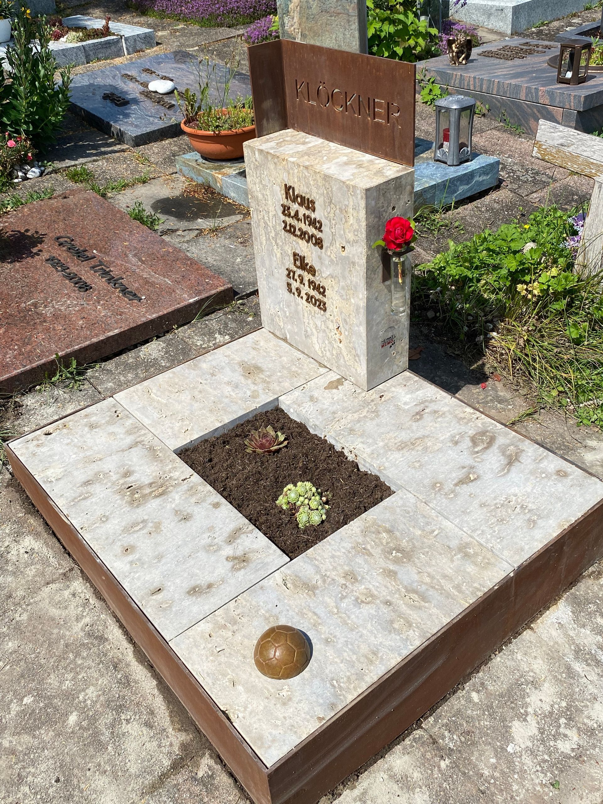 Ein Grab auf einem Friedhof mit einer roten Rose in einer Vase.