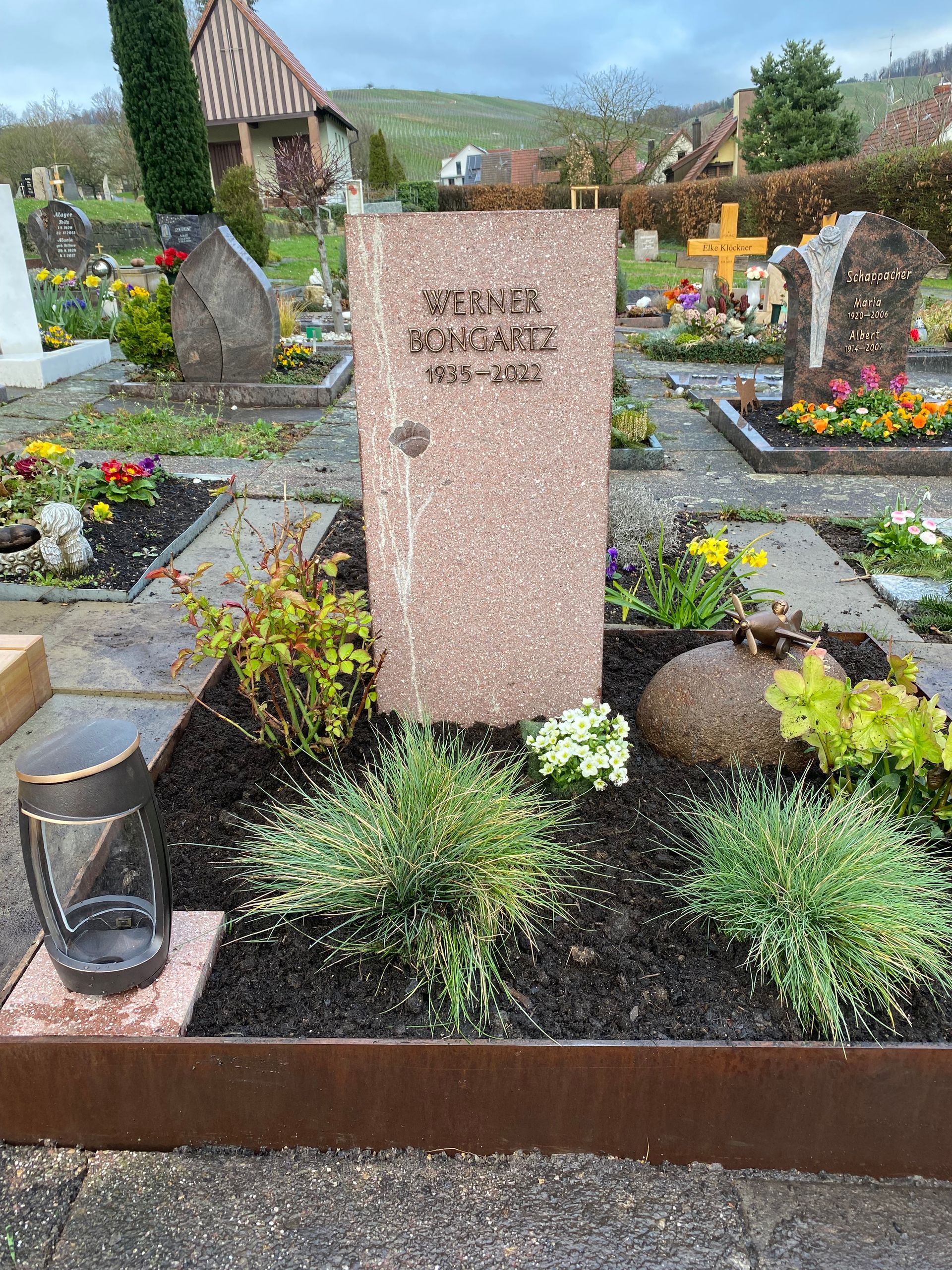Ein Grab auf einem Friedhof, umgeben von Blumen und Pflanzen.