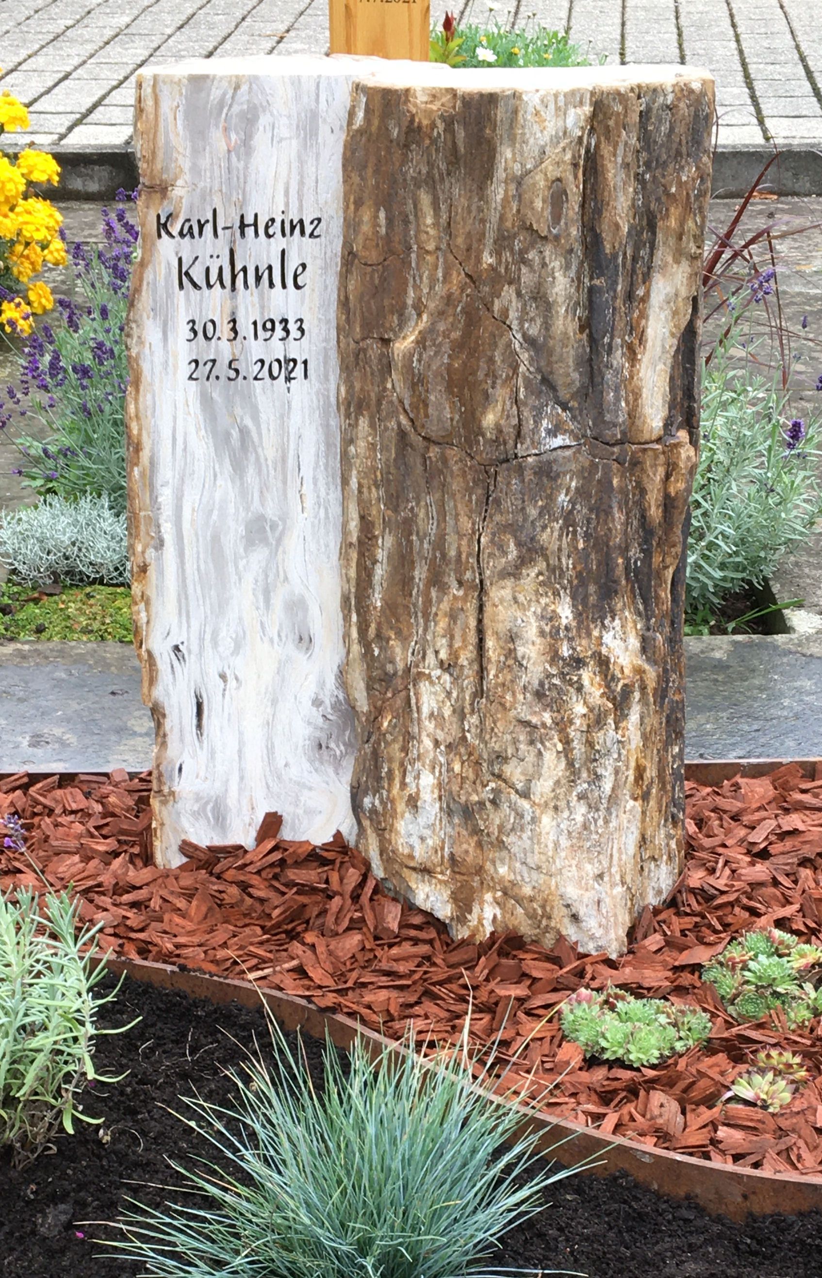 Ein aus einem Baumstumpf gefertigter Grabstein auf einem Friedhof.