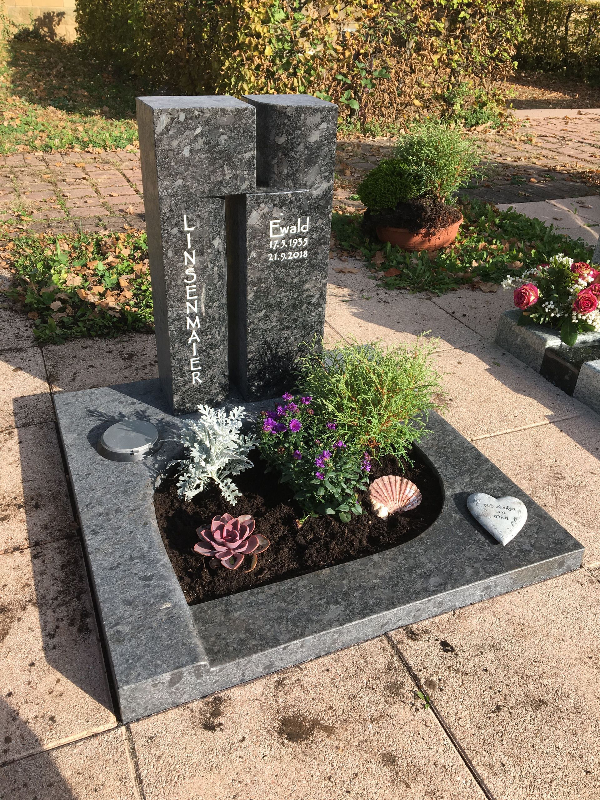 Ein Grab mit Blumen und einem Herz darauf auf einem Friedhof.