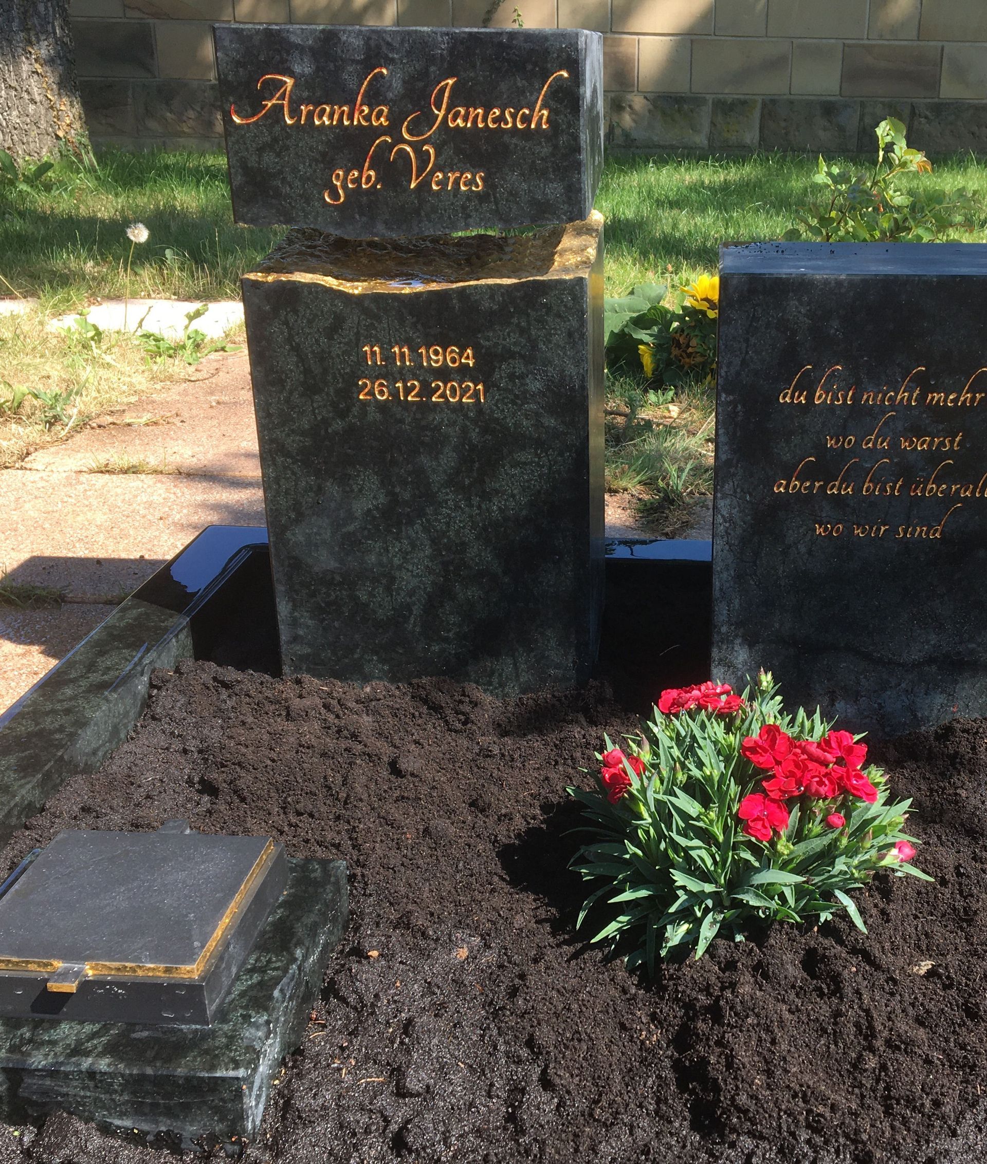 Ein paar Gräber auf einem Friedhof mit Blumen davor.