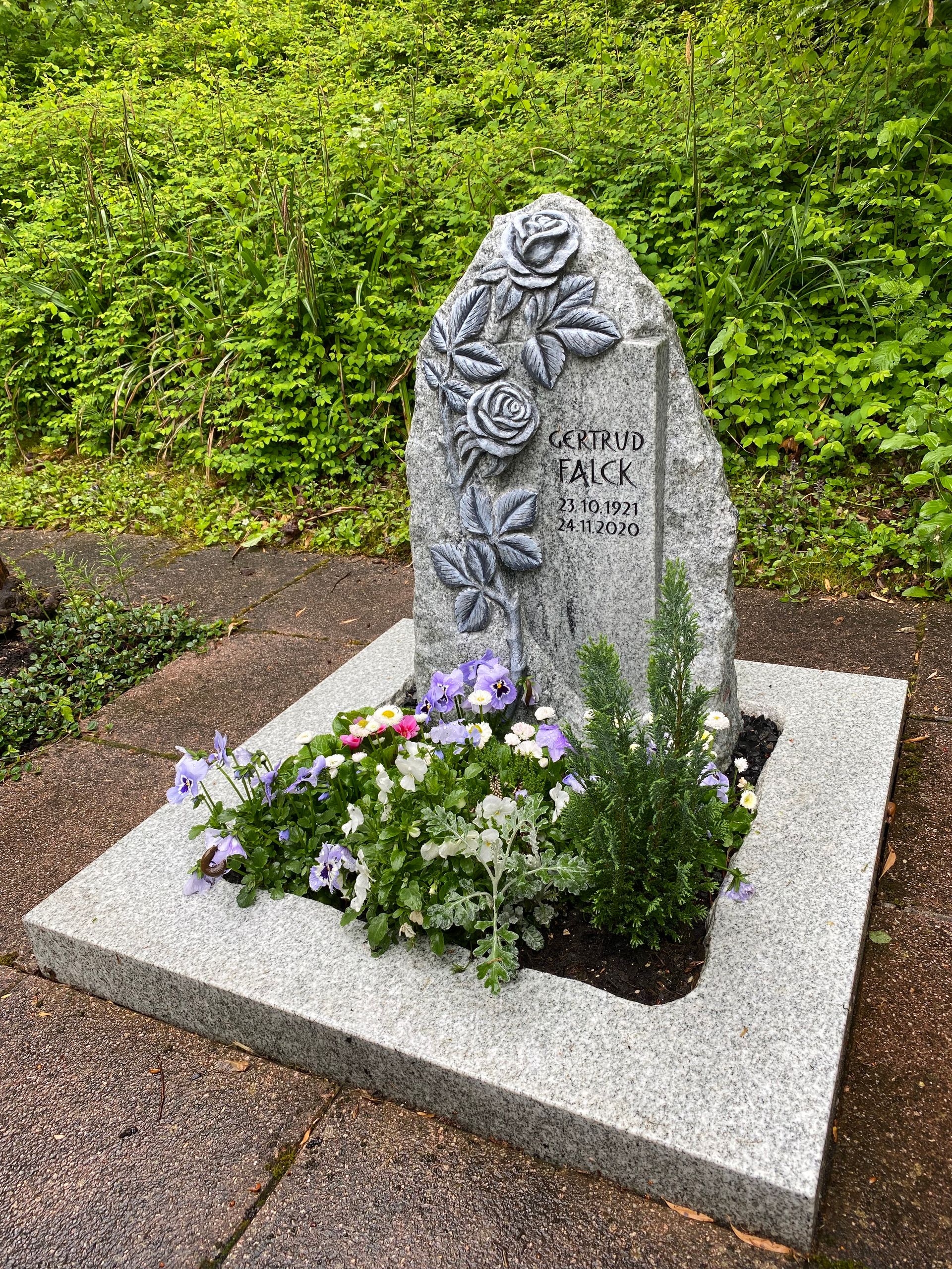 Auf einem Bürgersteig steht ein Grabstein mit Blumen darin.