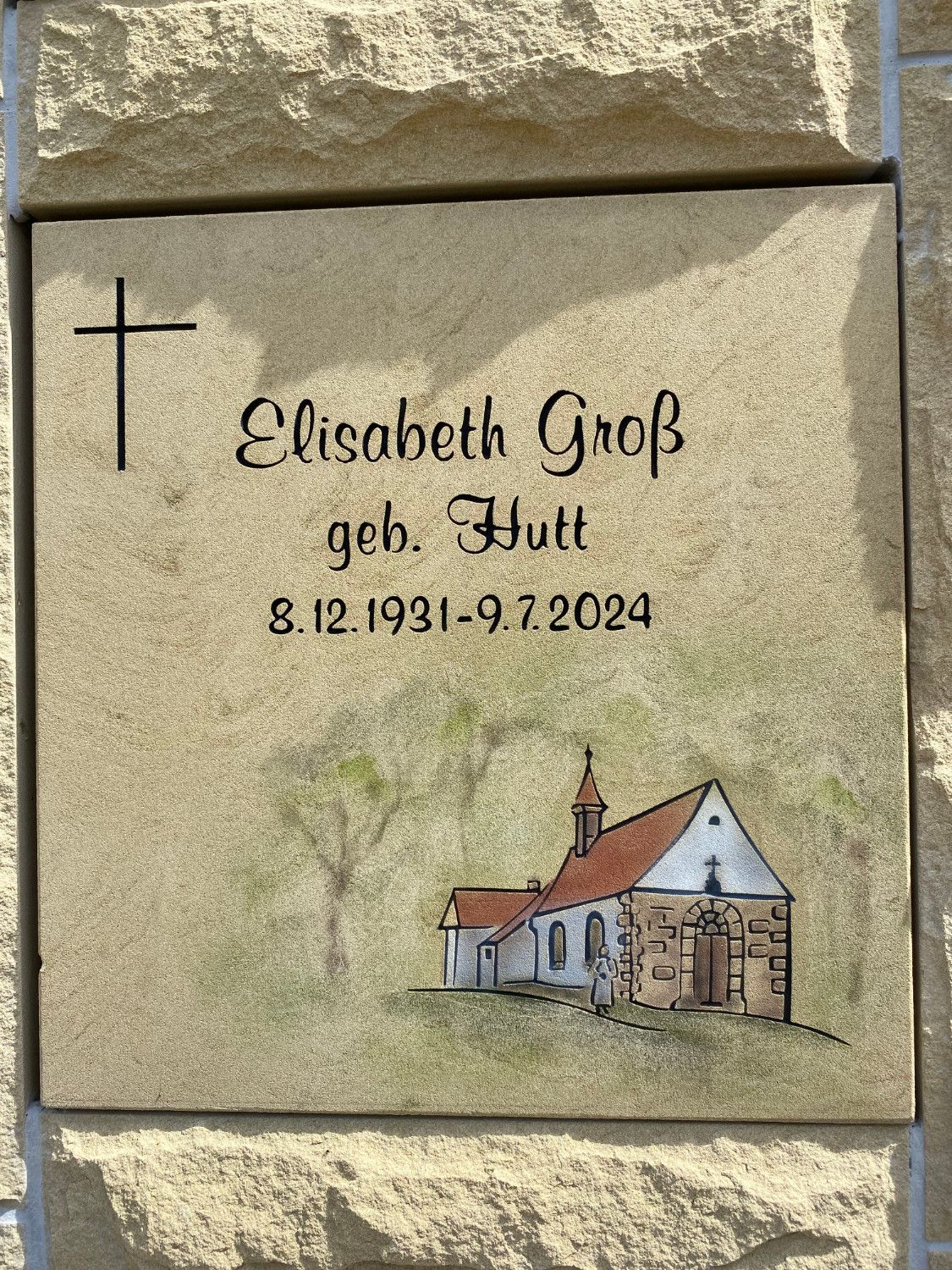 Ein Grabstein mit dem Bild einer Kirche und einem Kreuz darauf.