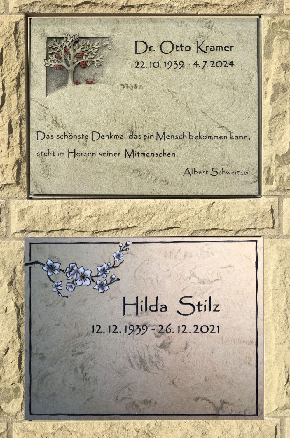 Ein paar Grabtafeln an einer Backsteinmauer.