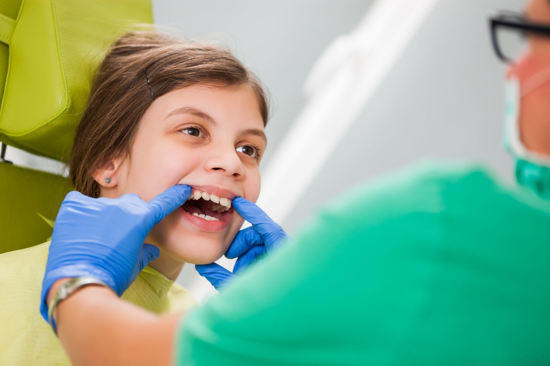 Una niña está sentada en una silla dental mientras un dentista le examina los dientes.
