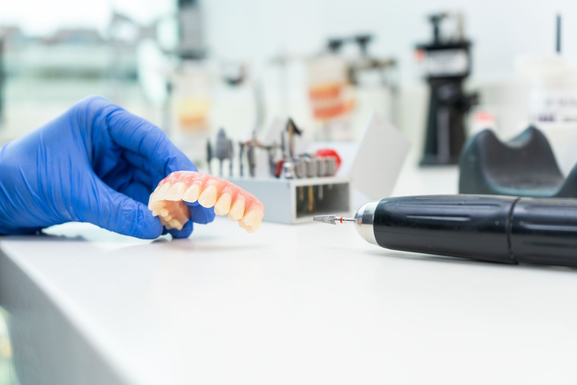 Una persona que lleva guantes azules sostiene una dentadura postiza en la mano.