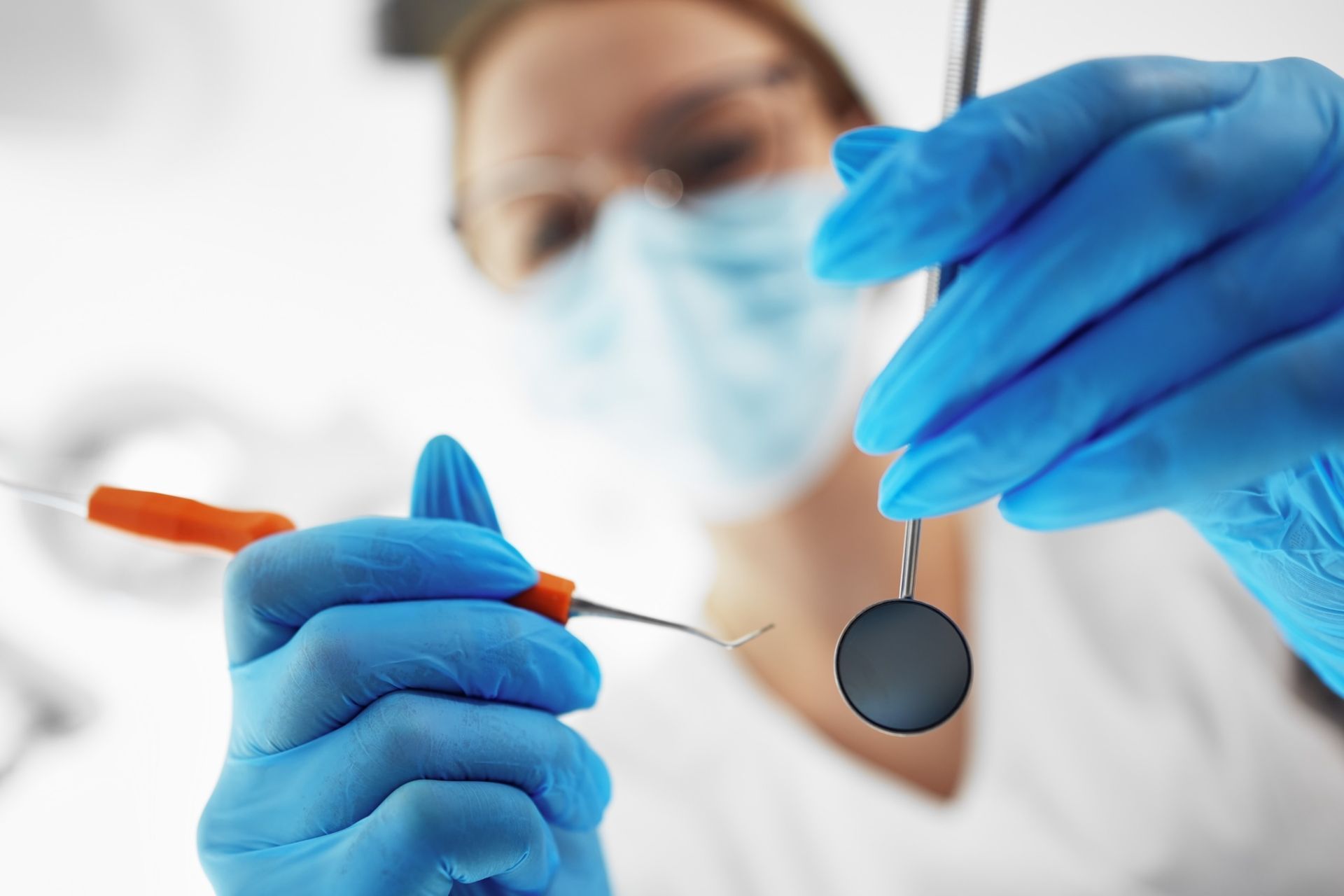 Un dentista que lleva una máscara y guantes azules sostiene una herramienta dental.