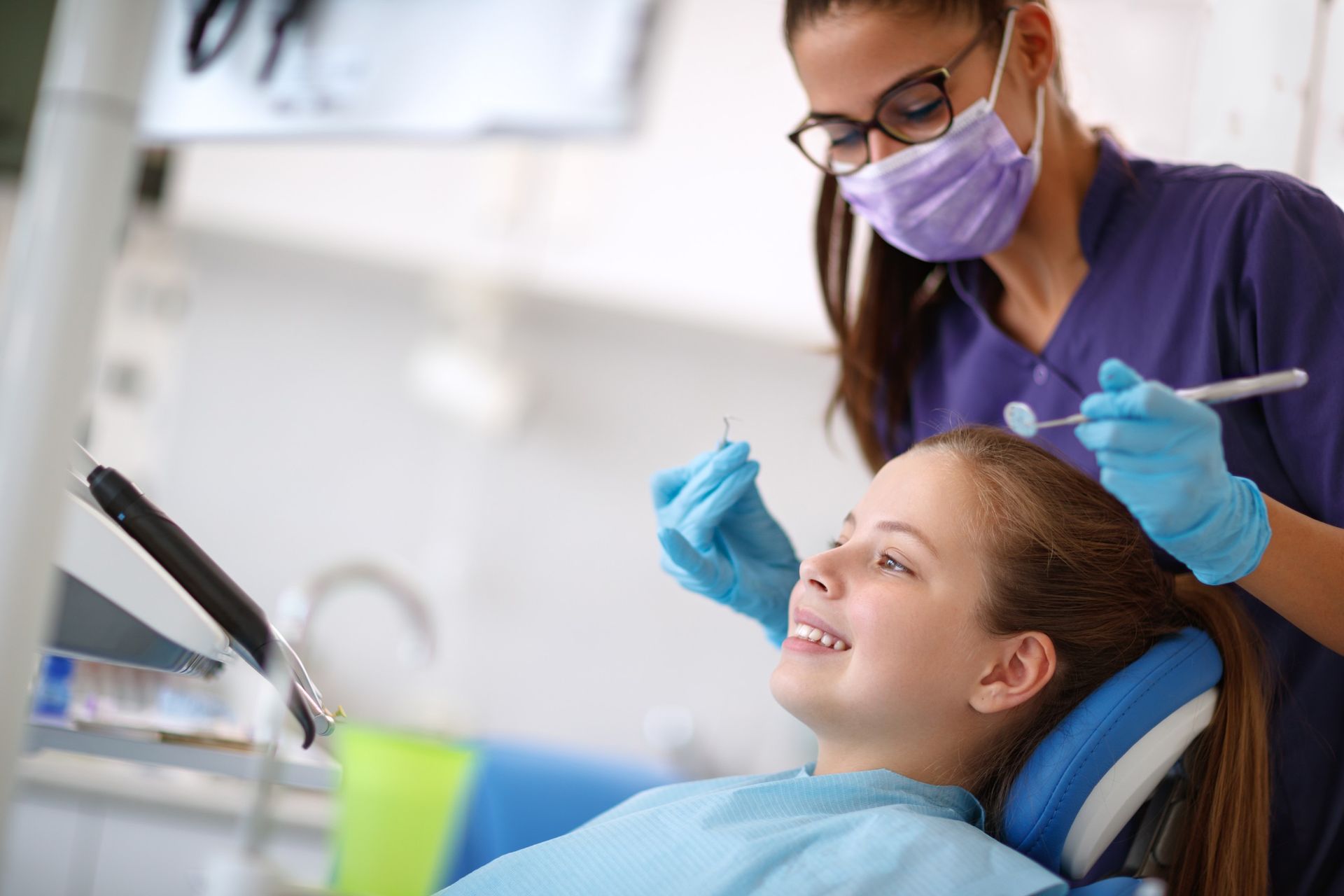 Una niña está sentada en una silla dental mientras un dentista le examina los dientes.