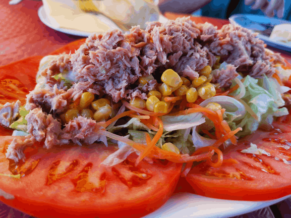 Una ensalada con atún, tomates, maíz y lechuga en un plato blanco.