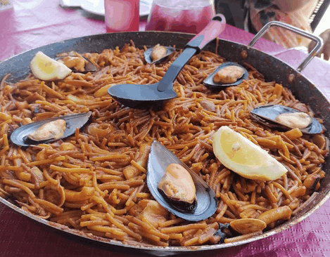 Una sartén de fideos con mejillones y rodajas de limón sobre una mesa.