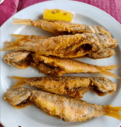 Un plato blanco cubierto con pescado frito y una rodaja de limón.