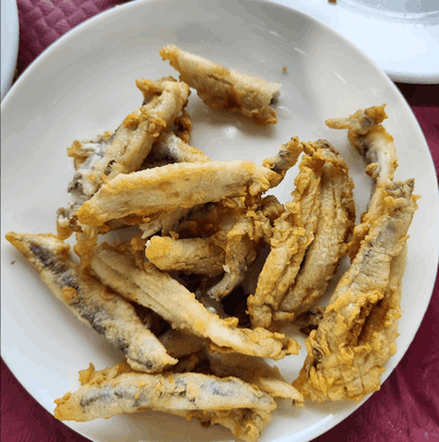 Un plato blanco cubierto con pescado frito sobre una mesa.