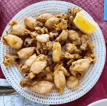 Un plato blanco cubierto con calamares fritos y una rodaja de limón.