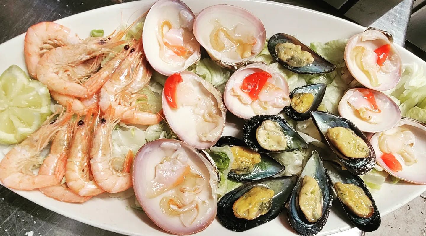 Un plato blanco cubierto con camarones, almejas y mejillones.
