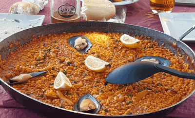 Una sartén de paella con rodajas de limón y mejillones sobre una mesa.