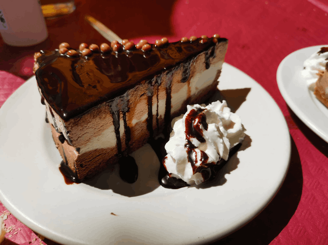 Una rebanada de tarta de queso con chocolate y crema batida en un plato blanco