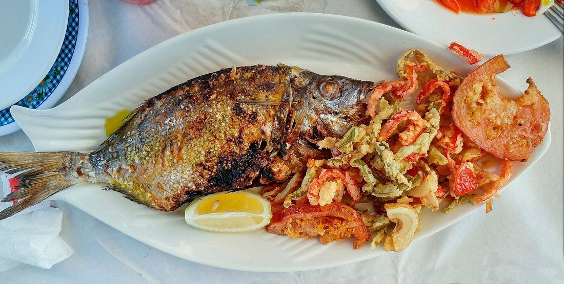 Un plato blanco cubierto con pescado y verduras sobre una mesa.
