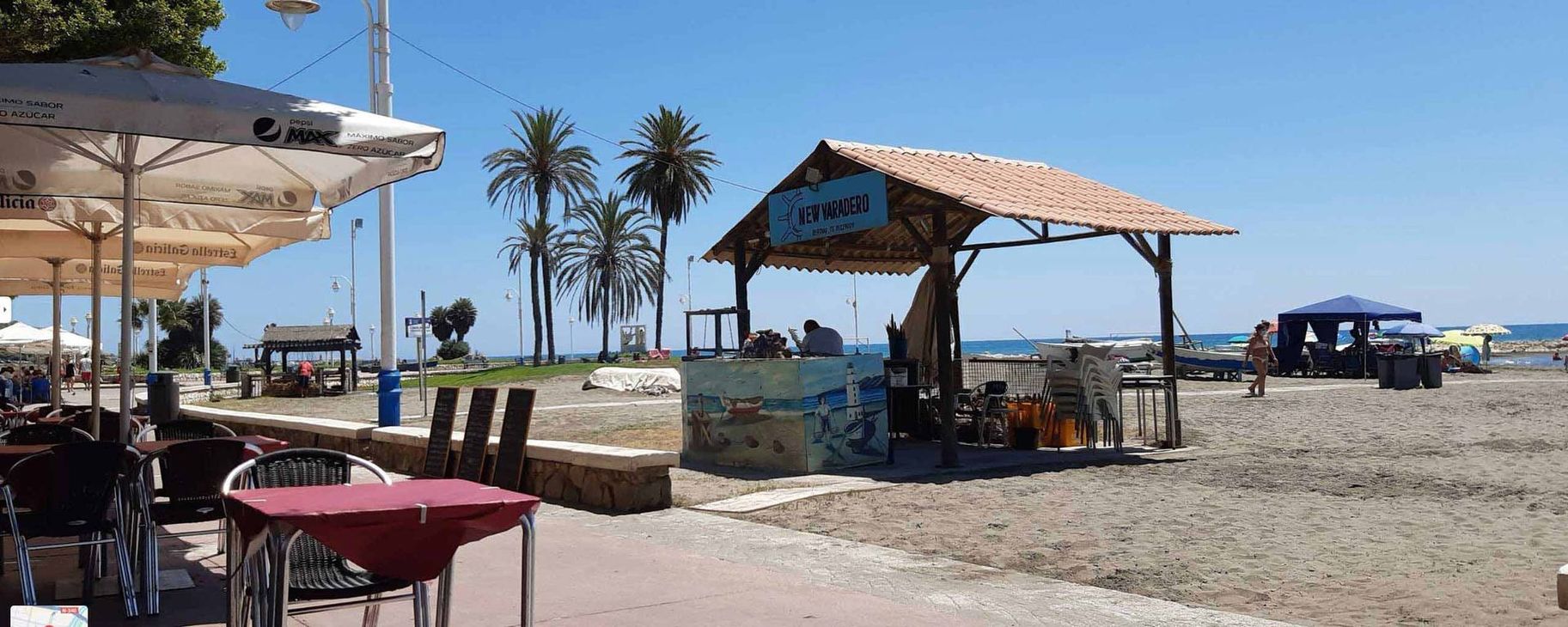 Una playa con mesas, sillas y sombrillas en un día soleado.