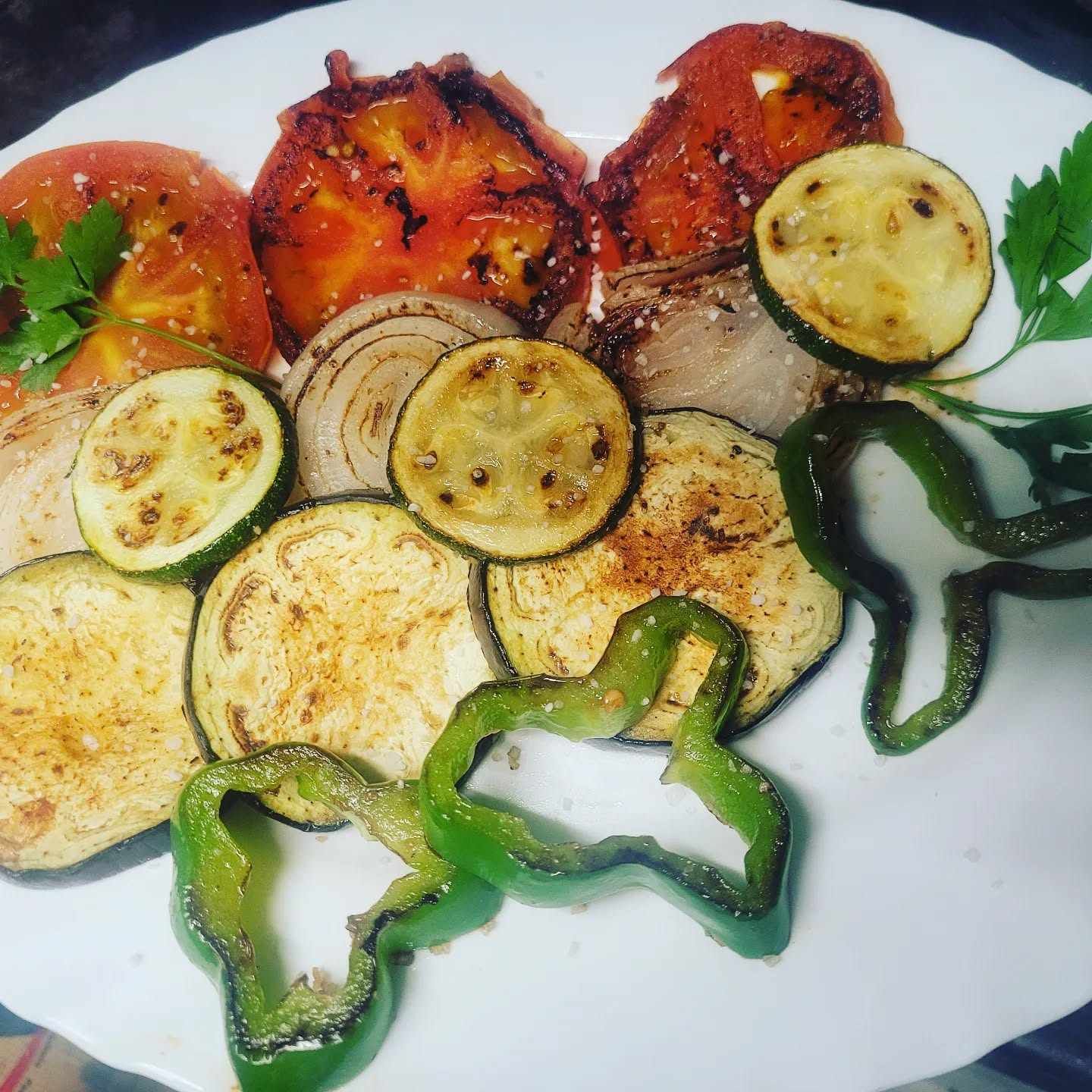 Un plato blanco cubierto con verduras a la parrilla, incluidos pimientos y tomates.
