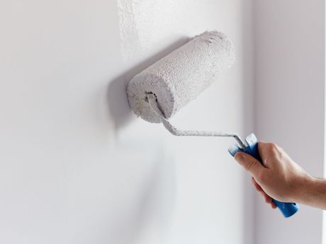 Main tenant un rouleau de peinture sur un mur blanc