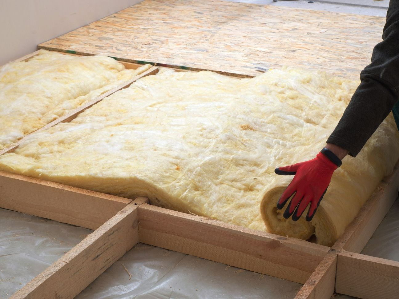 Pose de laine de verre sur un plancher bas par un artisan avec des gants rouges
