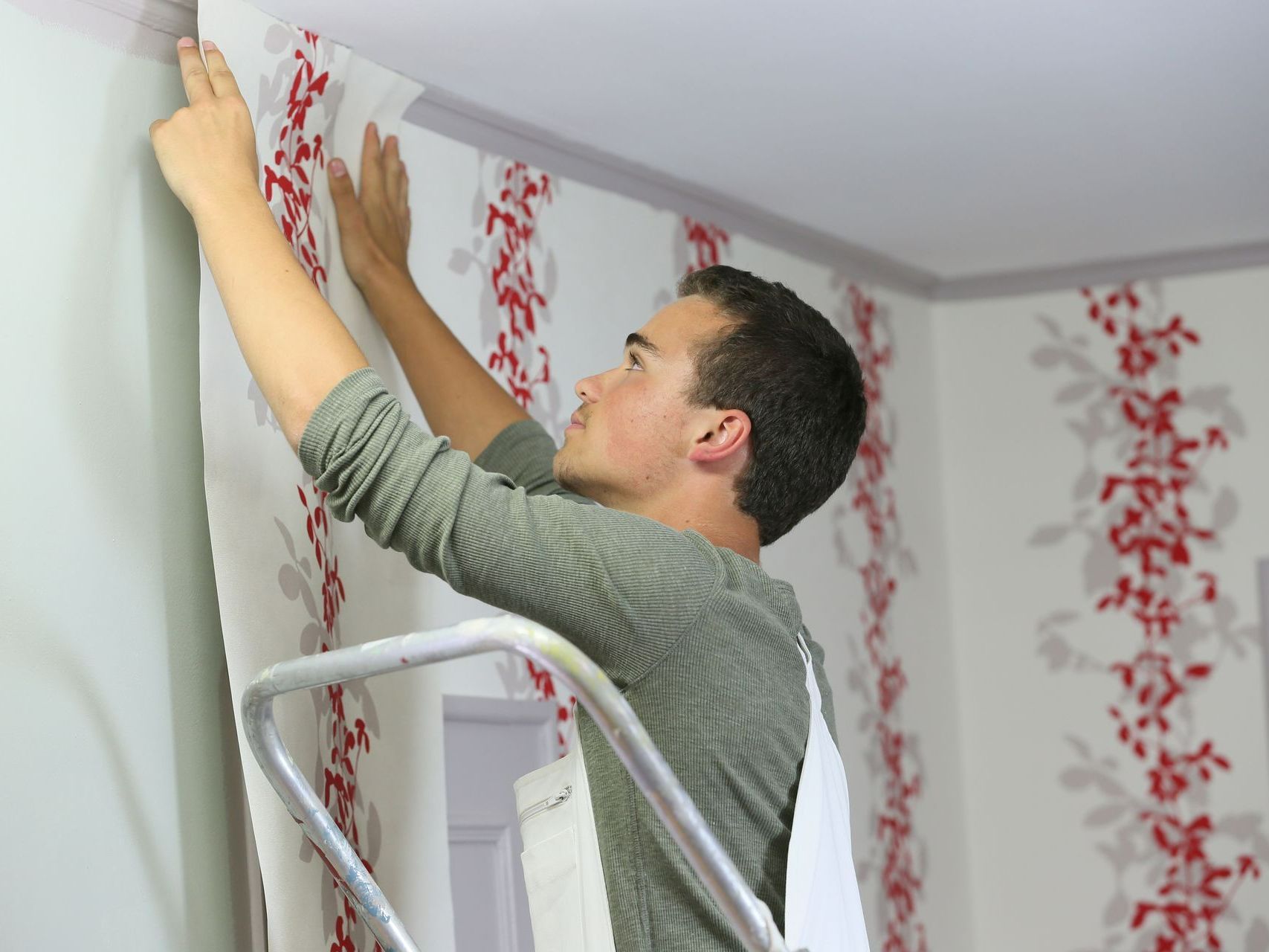 Un artisan applique une bande de tapisserie sur un mur