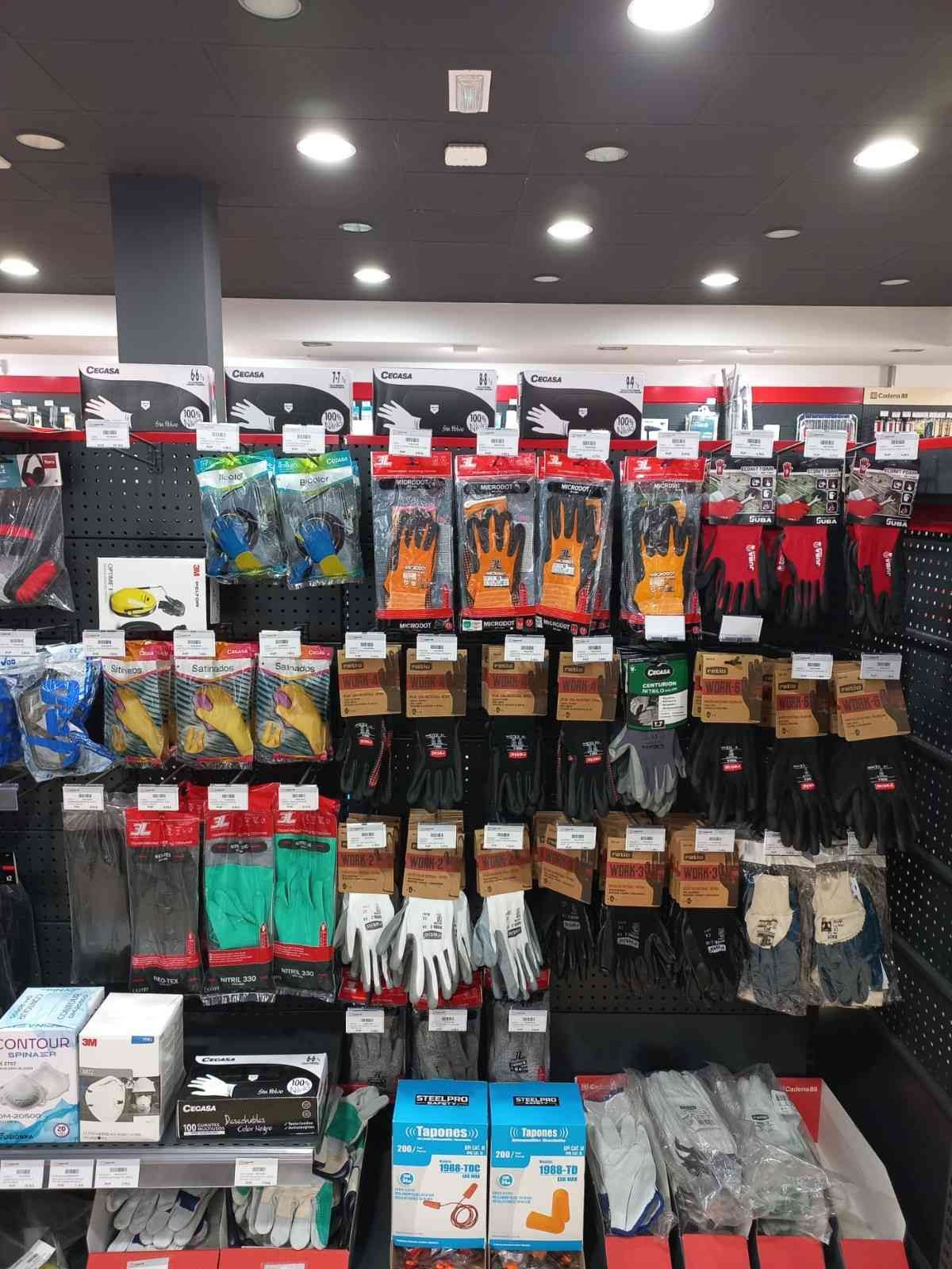 Estantes llenos de diversos guantes de trabajo en una tienda, incluidos guantes naranjas, blancos y rojos.