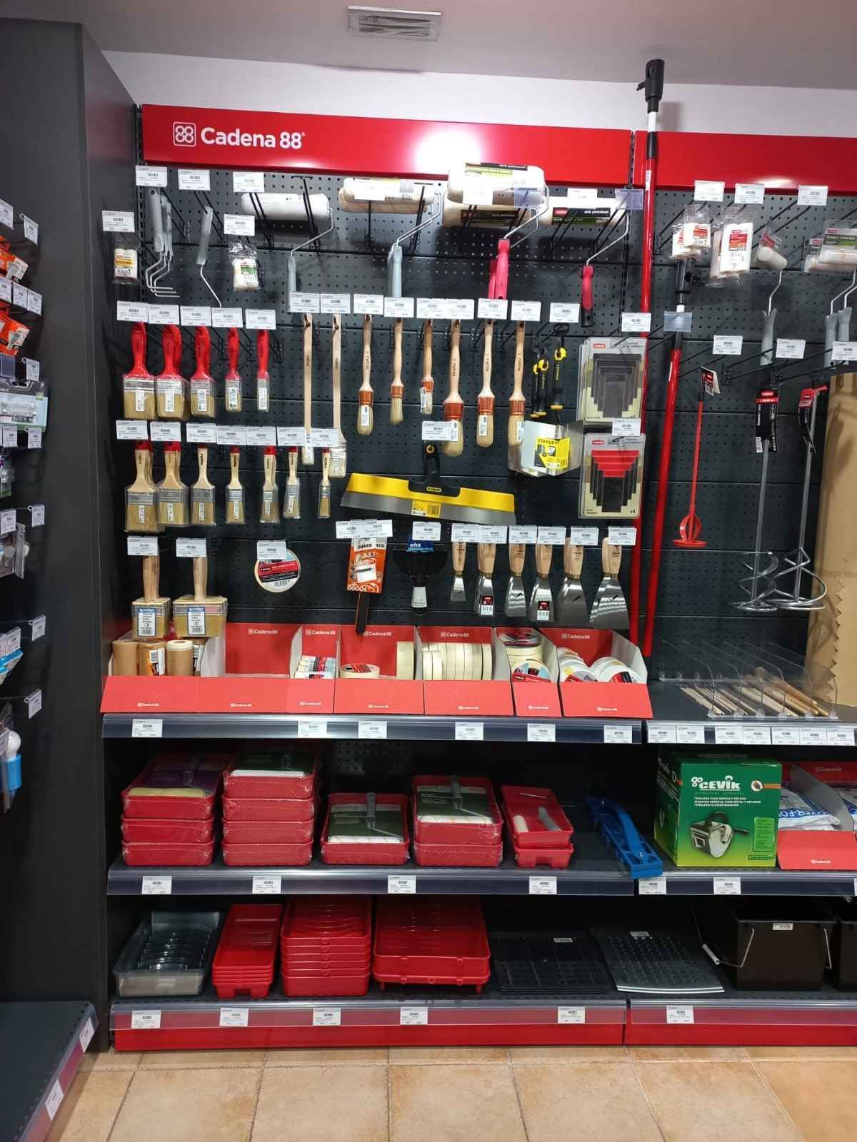 Pinceles y materiales expuestos en una tienda. Estanterías rojas y negras, pinceles de varios tamaños y bandejas de pintura.