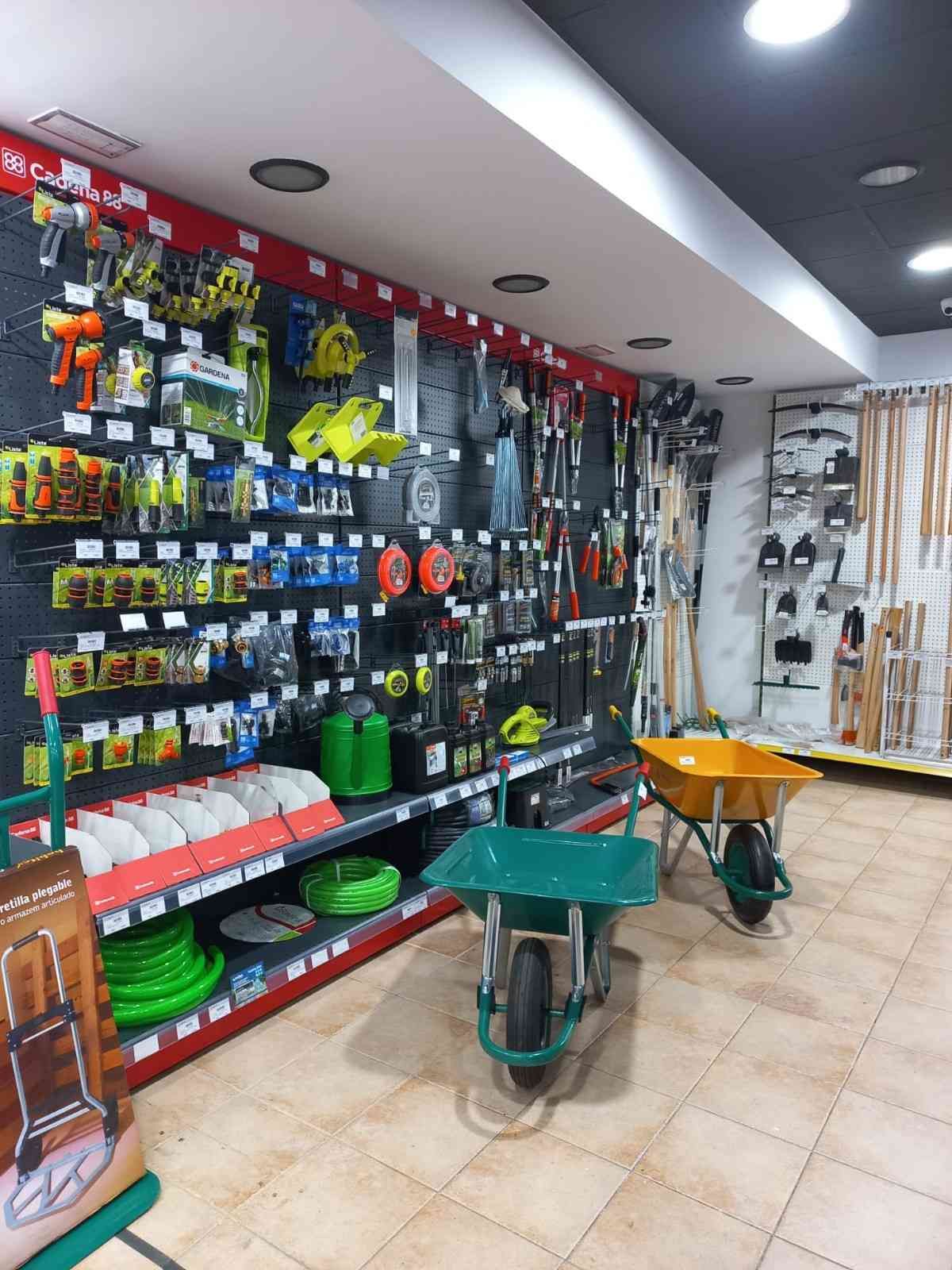 Interior de una ferretería con herramientas y artículos de jardinería en estantes y tableros perforados.